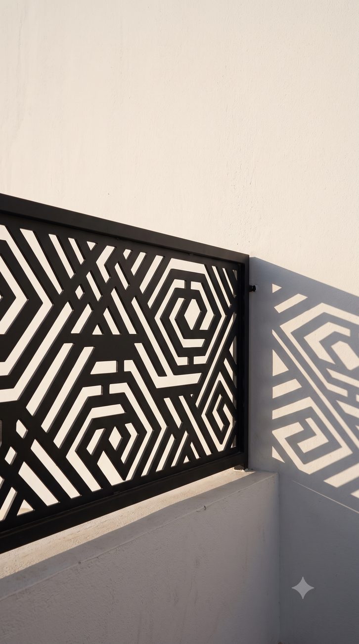 Détail d'un garde-corps claustra noir aux motifs géométriques, ombre portée sur le mur blanc — vue d'architecte
