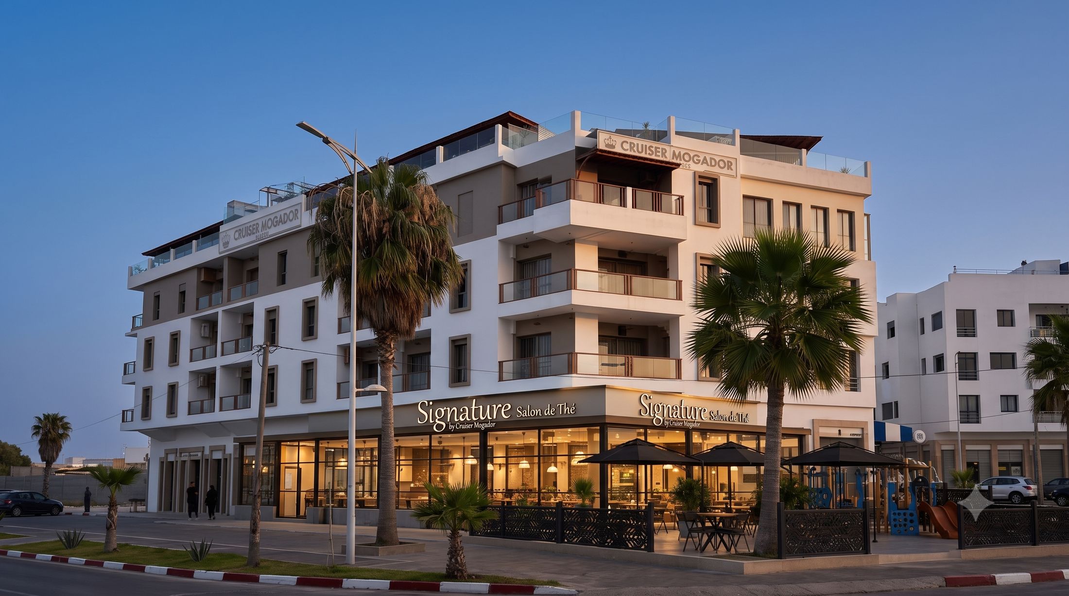 Le bâtiment Signature by Cruiser Mogador au crépuscule : façades blanches de l'hôtel, socle commercial éclairé, palmiers et terrasse — vue d'architecte