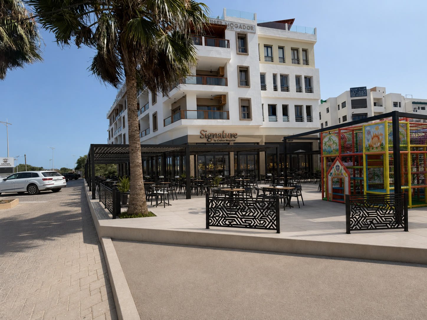 La grande terrasse de Signature by Cruiser Mogador à Essaouira, avec pergolas noires et aire de jeux